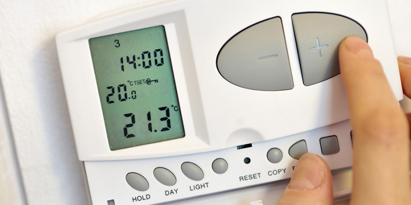 hand pressing button on digital thermostat